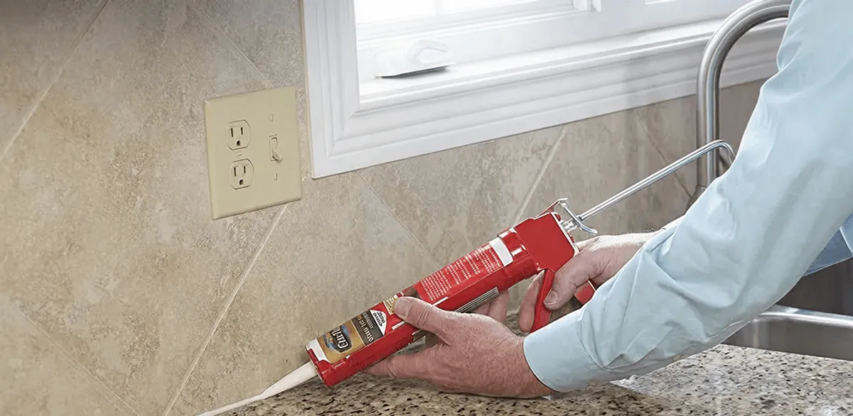 Handyman applying caulk along a kitchen backsplash and countertop seam in Syracuse, NY